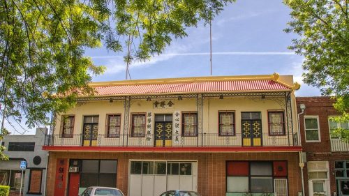Historic building with a red roof and decorative balcony, surrounded by trees and other storefronts.