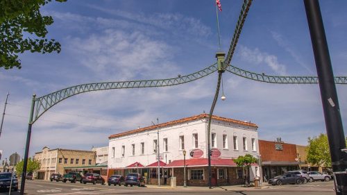A historic building with a white facade and awnings, under a decorative archway, in a small town setting.