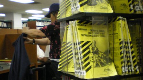 A library display of yellow pamphlets with black stripes, while a person organizes items in the background.