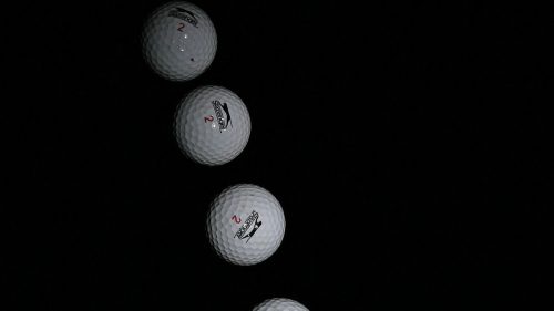 A sequence of six golf balls in motion against a dark background, showcasing their trajectory.