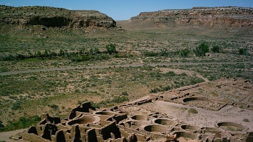 Ancient ruins nestled in a desert landscape, surrounded by rocky hills and sparse vegetation under a clear blue sky.
