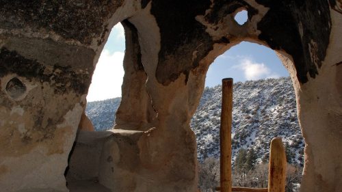 View through a stone archway, revealing a snowy landscape and wooden posts in the foreground.
