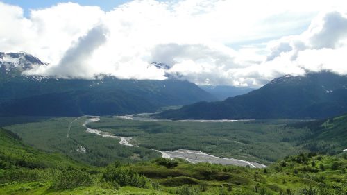A scenic view of a lush green valley surrounded by mountains and clouds, with a winding river flowing through.