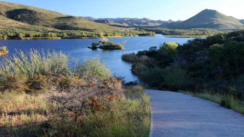 A serene landscape featuring a calm lake surrounded by hills and lush greenery under a clear blue sky.