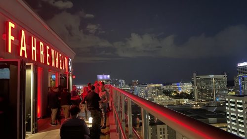 A rooftop bar named "Fahrenheit" at night, with people socializing and a city skyline illuminated in the background.