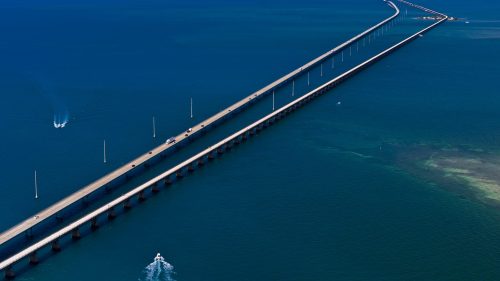 Aerial view of a long bridge extending over turquoise waters, with vehicles and boats visible.