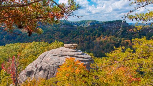 A rocky outcrop surrounded by vibrant autumn foliage and rolling hills under a partly cloudy sky.