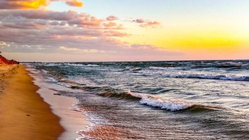 A serene beach at sunset, with gentle waves lapping at the shore and colorful clouds in the sky.