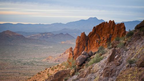 A rugged landscape featuring red rock formations and distant mountains under a soft, cloudy sky.