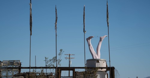 Looking toward a unique art display with a statue of legs sticking out of a barrel at an outdoor art museum in Joshua Tree, California.