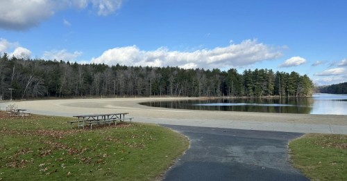 A wide view of the beach at the Long Pond in Grafton Lakes State Park, New York, with park benches on the beach and trees flanking the coast.