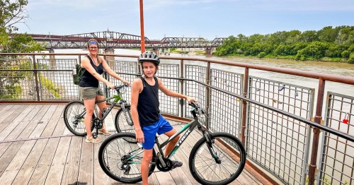 A mom and child on bikes overlooking the Missouri River during the summer, they are riding the Kansas City's Riverfront Heritage Trail, a rail trail in Missouri.
