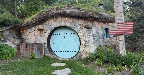 The exterior of the Maker’s Mark Hobbit House™ restaurant at The Preserve Sporting Club & Resort in Richmond, RI. The small building is made of stone and has a round, blue doorway.