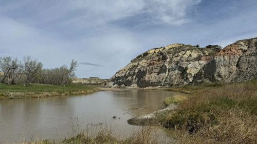 A rock formation sticking out of a prairie near a river.