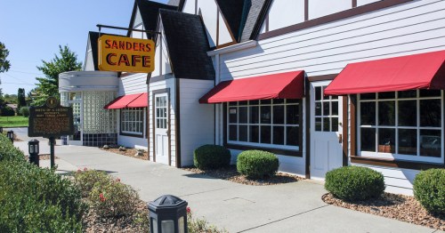 The facade of Sanders Cafe, a white-and-red restaurant with a neon sign in Corbin, Kentucky.