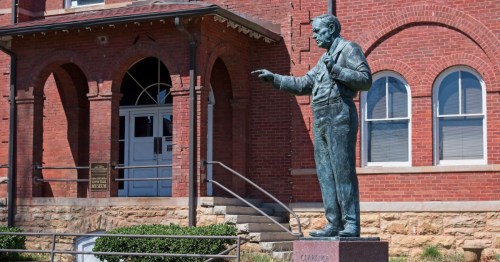 A bronze statue of Clarence Darrow outside a red courthouse building in Dayton, Tennessee.