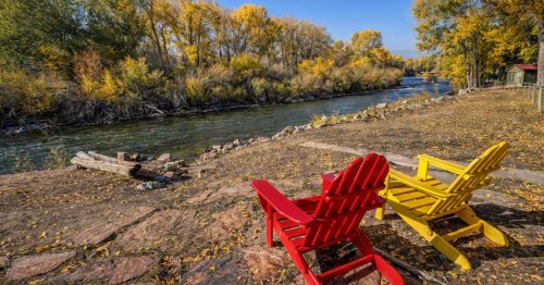 Two chairs sit next to a quiet river at a luxury Airbnb in Wyoming.