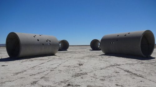 Four large concrete cylinders on a dry, cracked landscape under a clear blue sky.