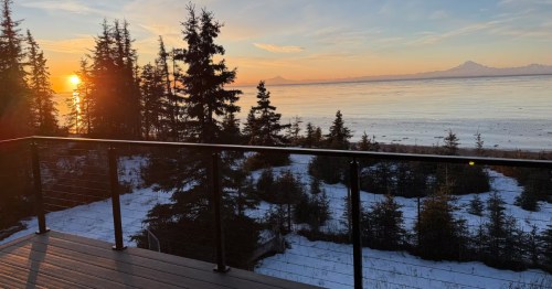 The sun sets over the Kenai Peninsula as seen from a deck on a waterfront Airbnb in Alaska.