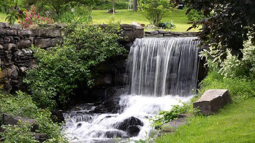 A serene waterfall cascading over rocks, surrounded by lush greenery and colorful flowers in a peaceful garden setting.