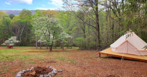 Secluded campsite in Georgia showing white tent on a camping platform with lots of space, fire pit, and ridge in the background.