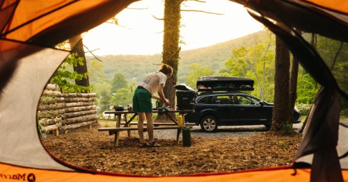 Perspective of a camper setting up a site as seen from an orange tent with a mountain ridge in the distance