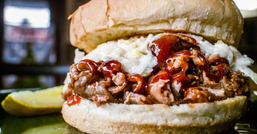 a carolina bbq sandwich with meat, sauce, and coleslaw with a pickle spear as a side