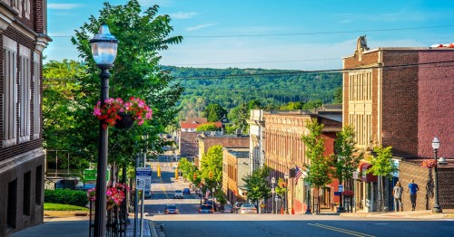 Hilly street view of downtown Marquette, Michigan, with flowering lamp posts and green trees on a summer day.