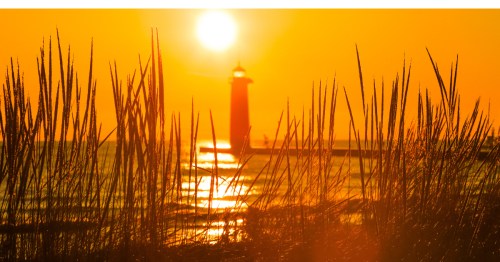 A golden sky with long beach grass in the foreground and a lighthouse in the background in Kenosha, Wisconsin