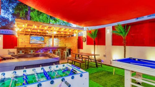 Outdoor recreational area featuring a foosball table, pool table, picnic table, and a hot tub under a red canopy.