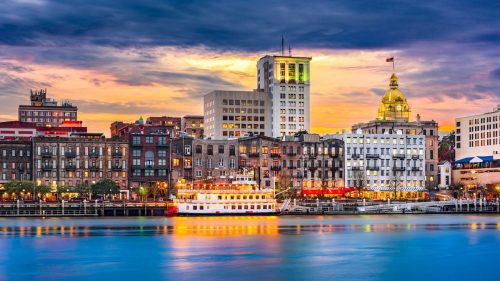 A scenic view of a city skyline at sunset, featuring historic buildings and a boat on the water.