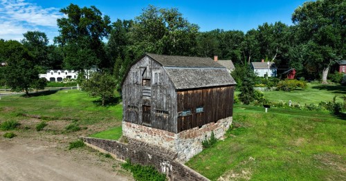 A very old wood building built on a concrete slab amongst greenery is seen in Wethersfield, MA.