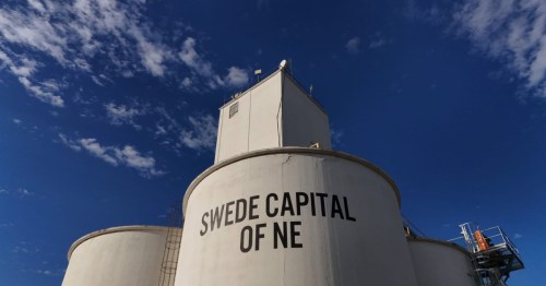 A dramatic low-angle shot of large white storage silos with the text "SWEDE CAPITAL OF NE" against a deep blue sky in Stromsburg, NE.