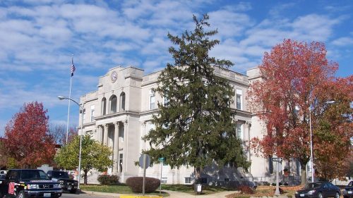 A historic building with a flag, surrounded by colorful autumn trees and parked cars under a blue sky.