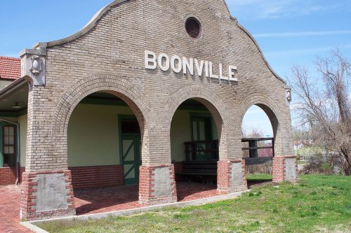 Historic Boonville train station with arched entrance and brick facade, surrounded by green grass and trees.