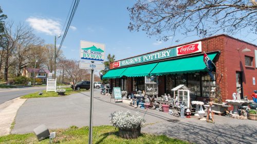 A pottery shop with a green awning, displaying various pottery items, next to a scenic byway sign on a sunny day.