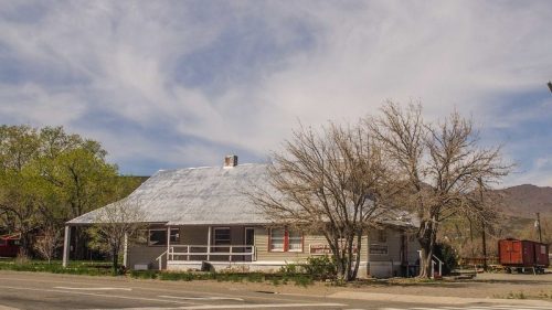 A quaint, single-story house with a metal roof, surrounded by bare trees and a clear blue sky with wispy clouds.