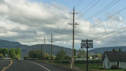 Road sign indicating East 140 and North 39, with power lines and hills in the background under a cloudy sky.