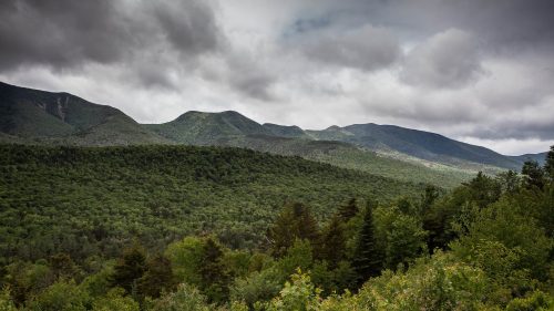 A panoramic view of lush green mountains under a cloudy sky, showcasing a serene natural landscape.