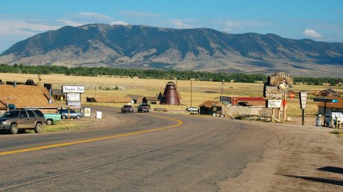 A scenic view of a rural road leading to a small town, with mountains in the background and a clear blue sky.