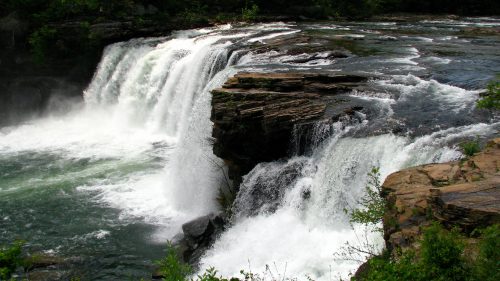 A scenic waterfall cascading over rocky cliffs, surrounded by lush greenery and flowing into a river below.