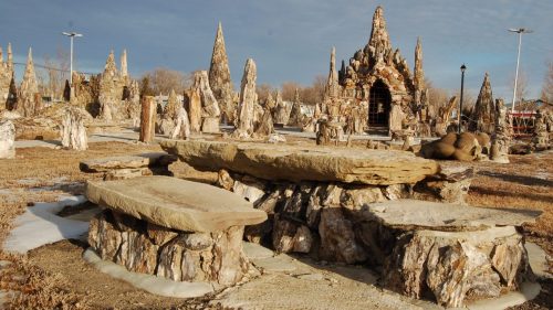 A unique outdoor landscape featuring rock formations, sculptures, and a stone seating area under a cloudy sky.