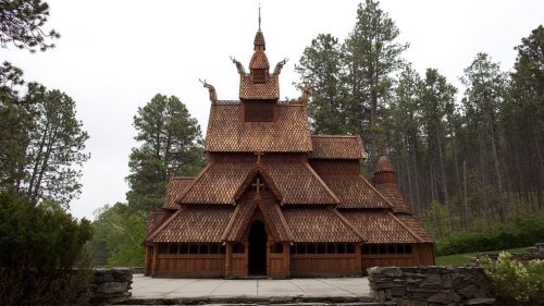 A wooden church with intricate architecture, surrounded by tall trees and greenery.