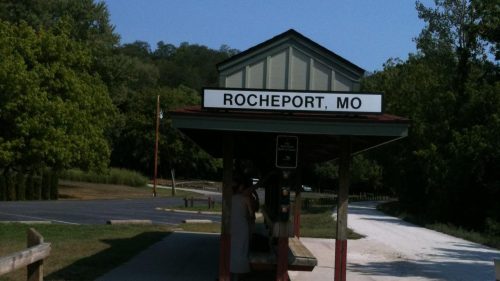 A small train station in Rocheport, MO, surrounded by trees and a clear blue sky.