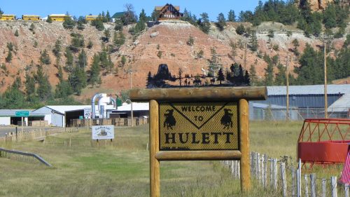 Welcome sign for Hulett, Wyoming, with a scenic backdrop of hills and buildings in the distance.