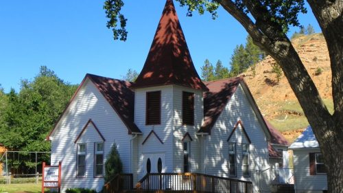 A quaint white church with a red steeple, surrounded by trees and a clear blue sky.