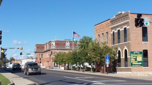 A street view featuring brick buildings, traffic lights, and an American flag, with clear blue skies above.