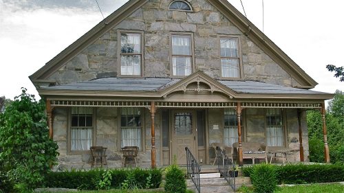 Historic stone house with a gabled roof, front porch, and the year "1841" displayed above the entrance.