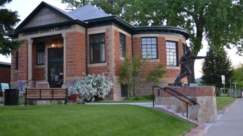 Historic building of the Jackson County Library, featuring a statue and lush green landscaping.