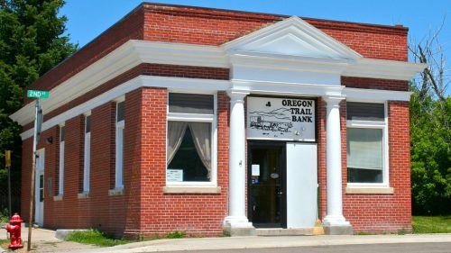 Brick building with white columns and a sign reading "Oregon Trail Bank," set against a clear blue sky.